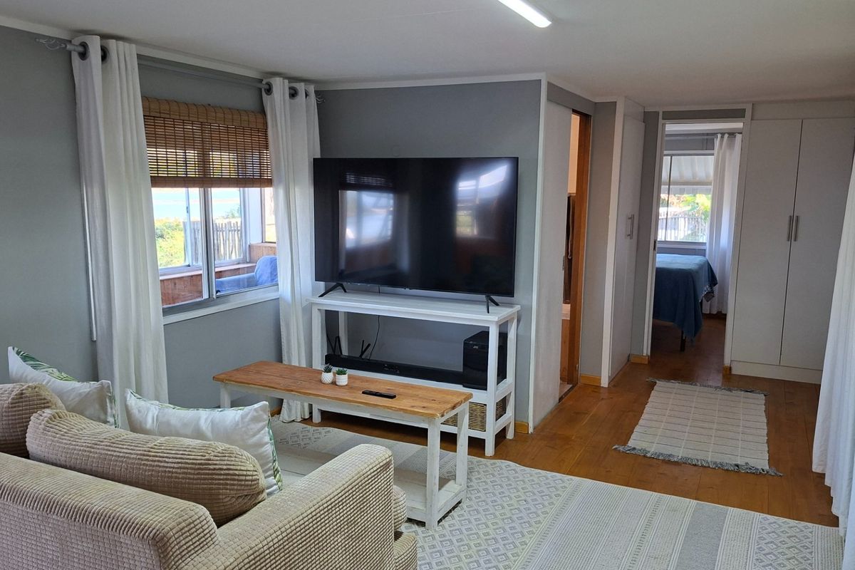 A comfortable living room featuring timber flooring, neutral wall tones, and direct access to an adjacent bedroom with built-in storage.
