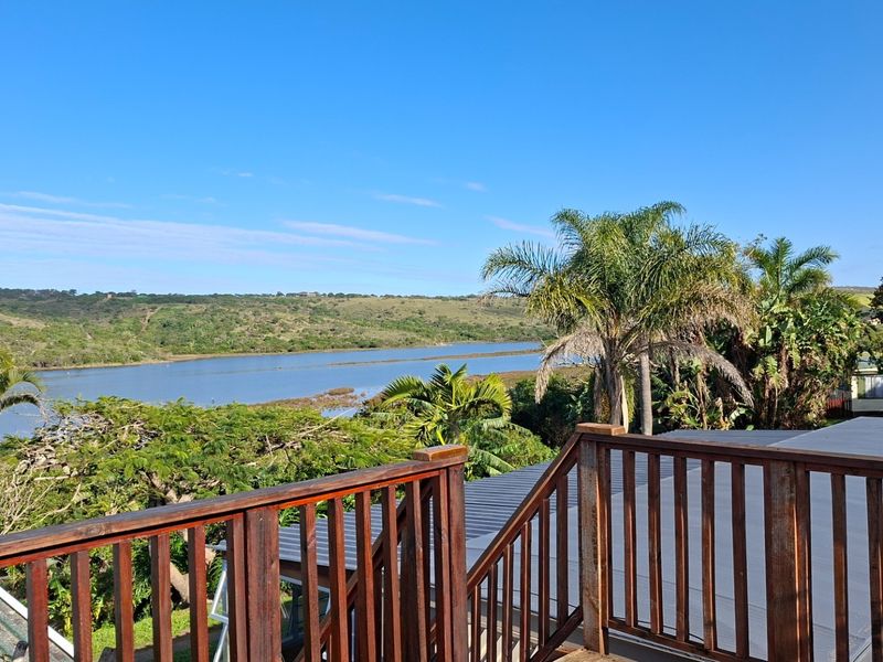 Elevated view overlooking a scenic lagoon and surrounding natural landscape, featuring a wooden deck railing in the foreground.