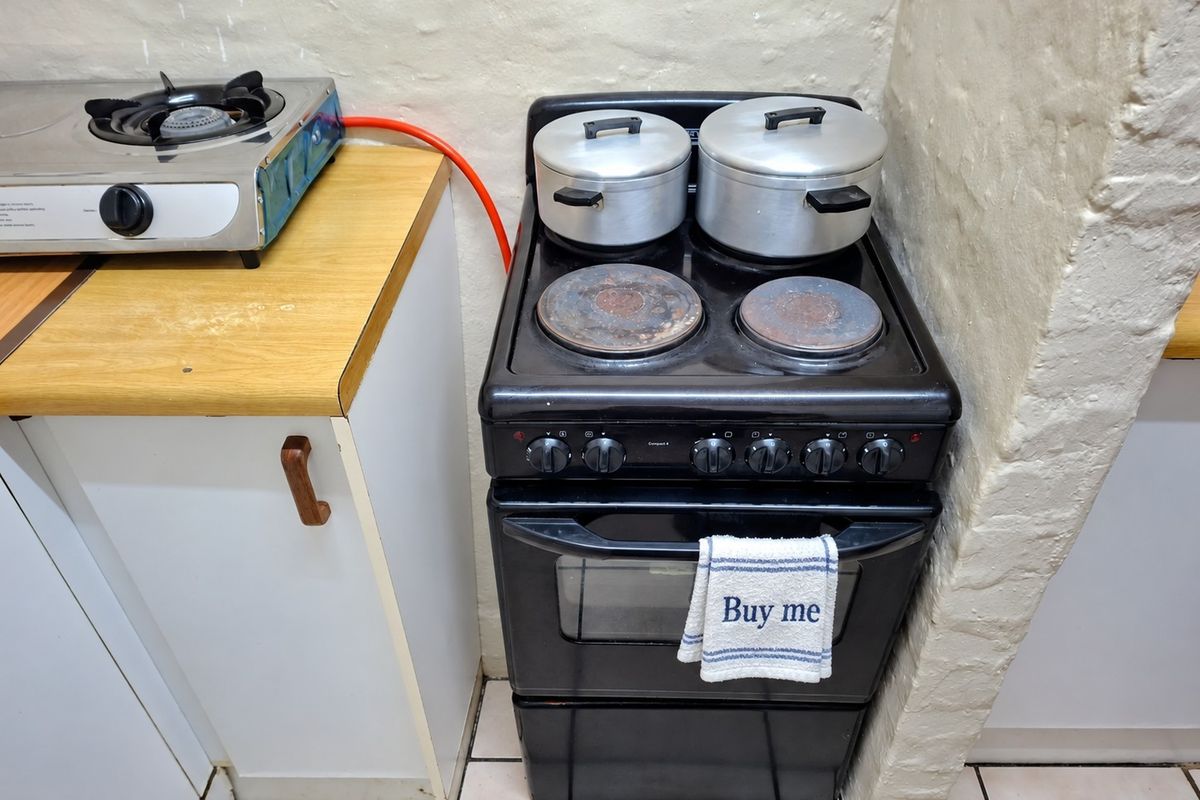 A compact kitchen area featuring a freestanding electric stove, a secondary gas hob, laminate countertops, and tiled flooring.