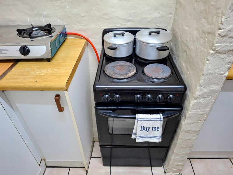 A compact kitchen area featuring a freestanding electric stove, a secondary gas hob, laminate countertops, and tiled flooring.