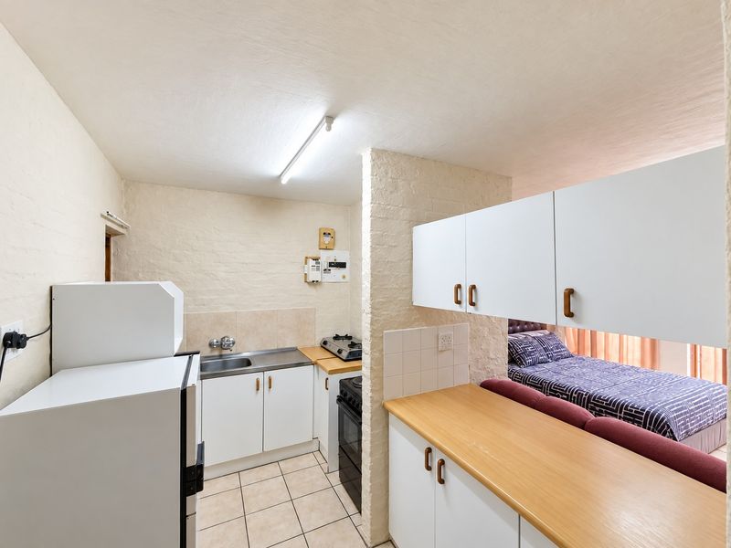 Compact open-plan kitchen area featuring white cabinetry, stainless steel sink, and tiled flooring, seamlessly connected to the adjacent bedroom space.