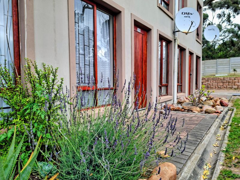 Front facade of a residential unit featuring timber doors and window frames with security bars, complemented by a paved walkway and landscaped garden.