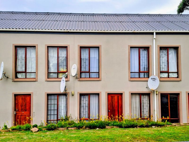 Front elevation of a multi-unit residential building featuring timber-framed windows with security bars, wooden doors, and multiple satellite dish installations.