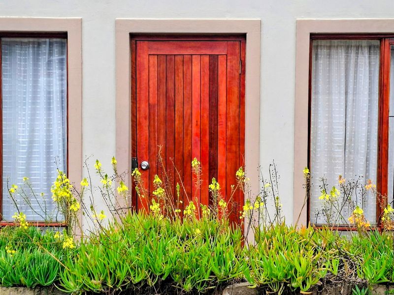 A front facade view featuring a solid timber door flanked by two windows with neutral framing and a well-maintained plastered exterior wall.