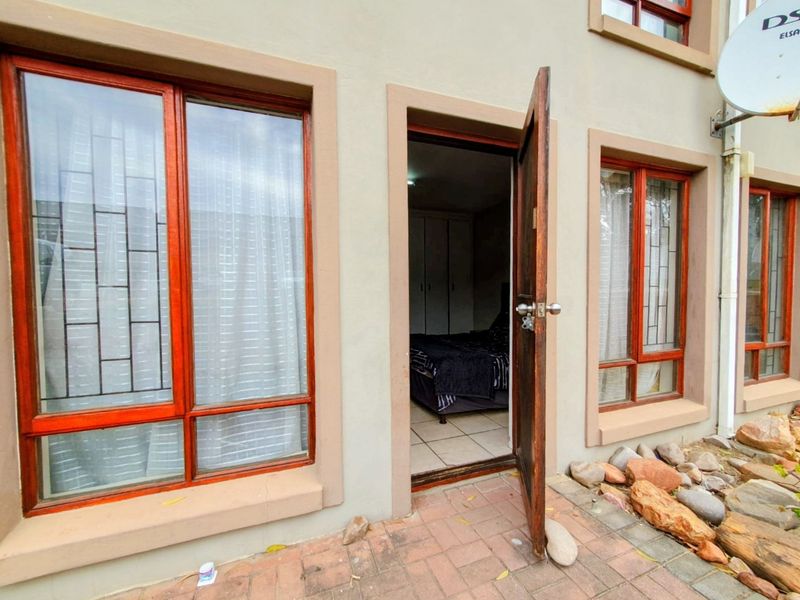 Exterior view of a rear patio featuring timber-framed windows with security bars, leading into a bedroom with built-in cupboards.