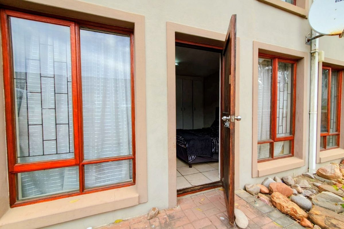 Exterior view of a rear patio featuring timber-framed windows with security bars, leading into a bedroom with built-in cupboards.