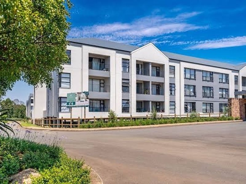 A modern multi-story apartment complex featuring a paved driveway, stone facade accents, and private balconies for each unit.