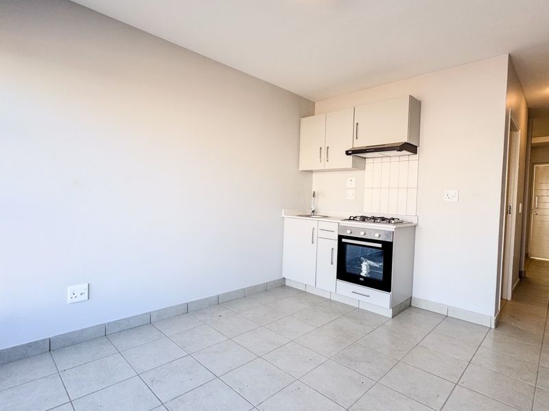 A compact, modern kitchen area featuring built-in cabinetry, a gas hob, oven, and extractor fan, set against neutral tiled flooring.