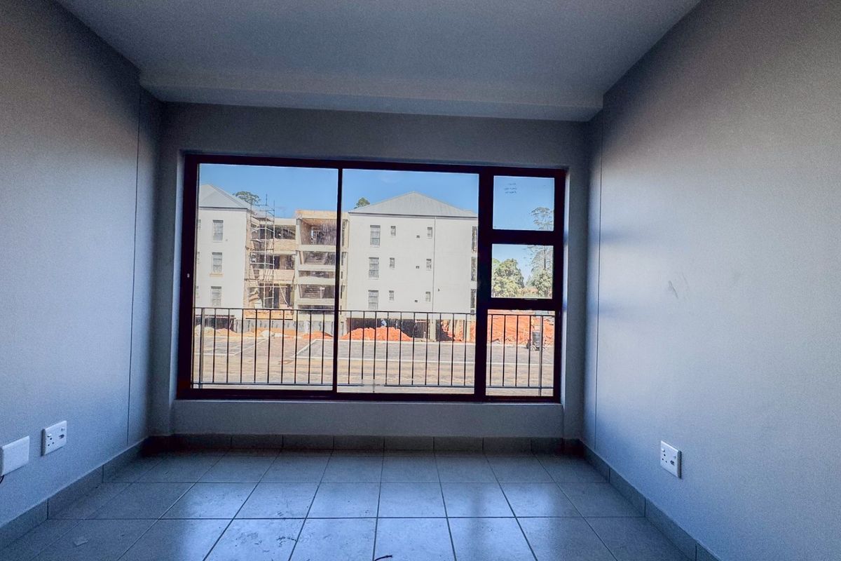 A bright, empty bedroom featuring tiled flooring, neutral walls, and a large window providing natural light and an exterior view.