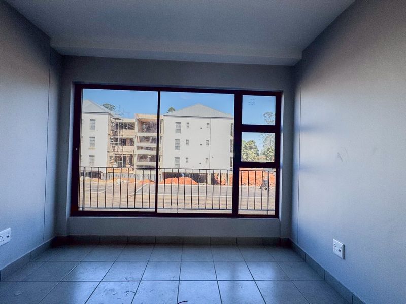 A bright, empty bedroom featuring tiled flooring, neutral walls, and a large window providing natural light and an exterior view.