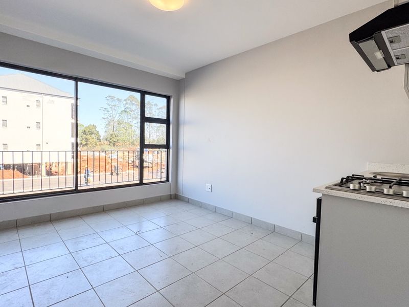 An open-plan kitchen and living area featuring tiled flooring, a gas hob with extractor, and large windows providing natural light and exterior views.