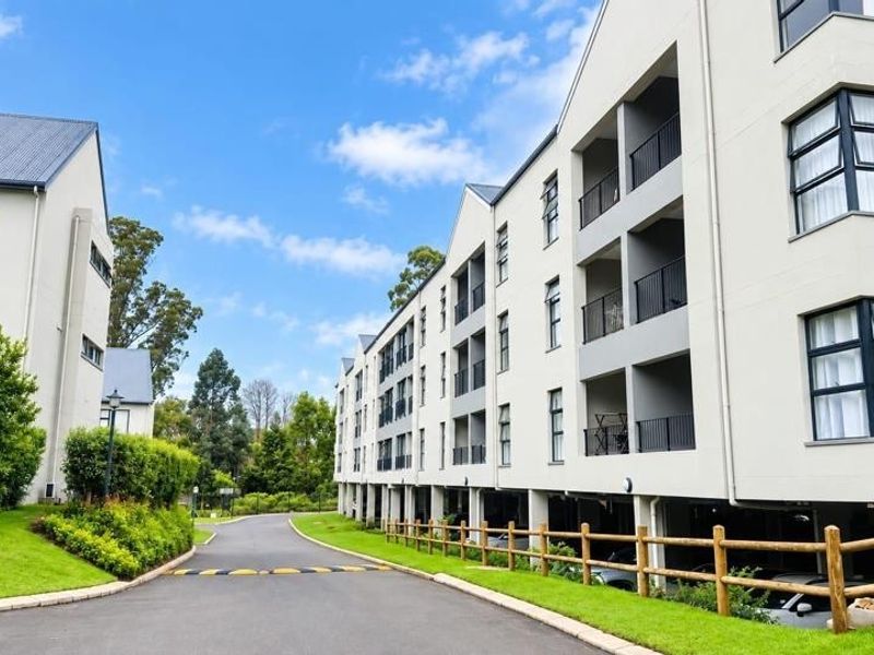 A view of the apartment complex exterior featuring a paved driveway, landscaped gardens, and multi-level balconies with metal railings.