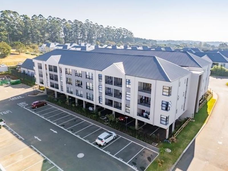 Aerial view of a modern multi-story apartment complex featuring a paved parking area and well-maintained building exterior.