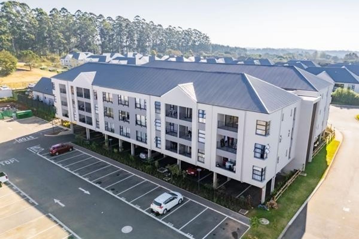 Aerial view of a modern multi-story apartment complex featuring a paved parking area and well-maintained building exterior.