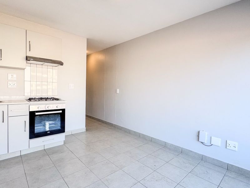 A clean, open-plan kitchen area featuring white cabinetry, a gas hob, built-in oven, and neutral tiled flooring, ready for personalization.
