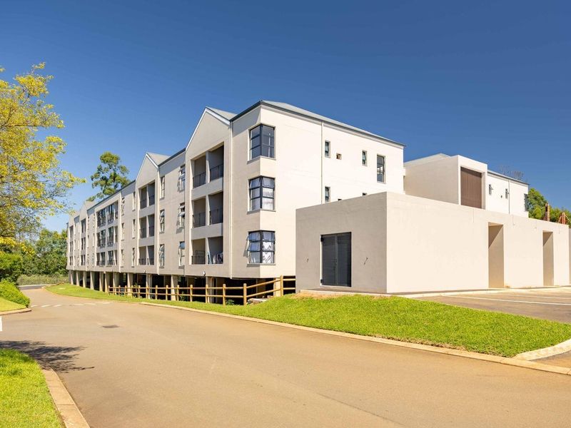 A clear exterior view of a modern multi-story apartment complex featuring paved driveway access, landscaped grounds, and private balconies.