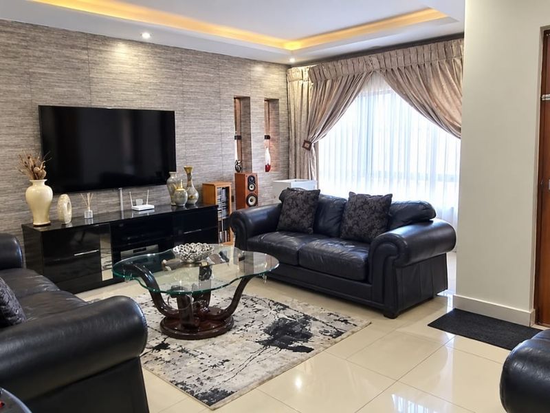 A well-maintained living room featuring polished tile flooring, a textured feature wall, recessed ceiling lighting, and a solid wood entrance door.