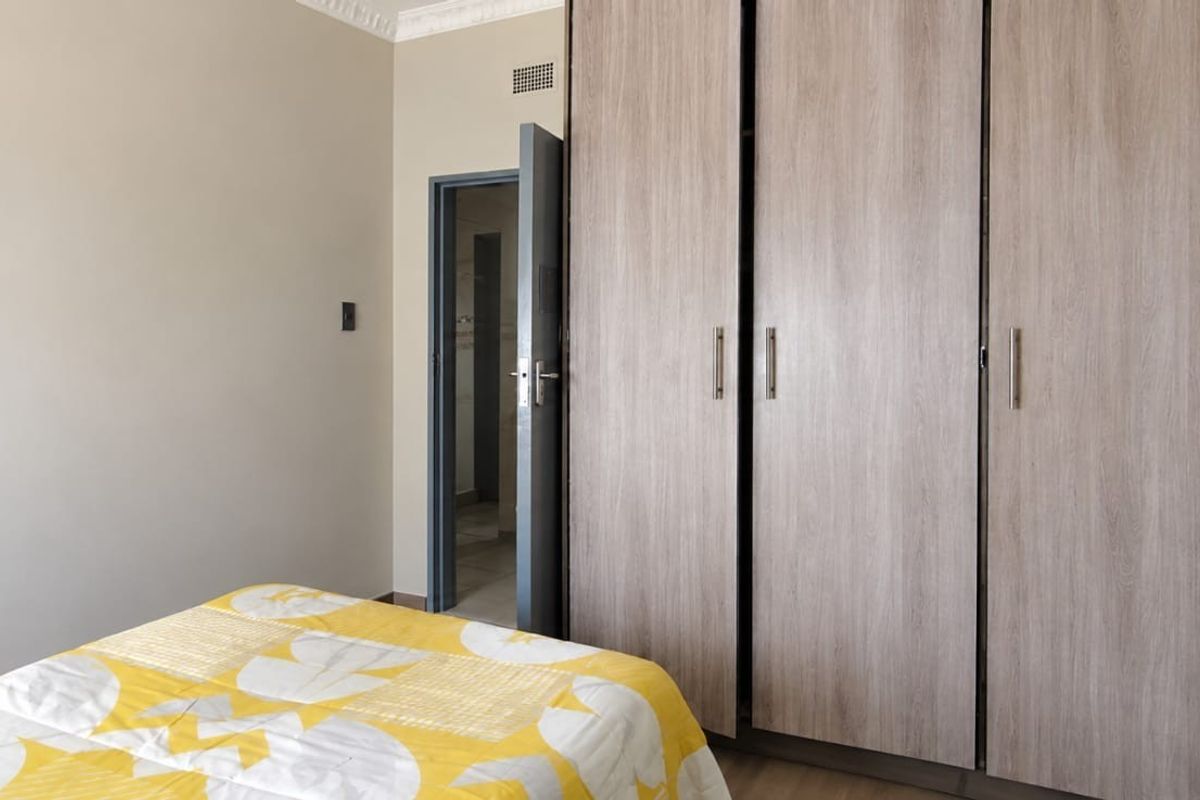 A bedroom featuring light wood-finish built-in cupboards, decorative ceiling cornice, and laminate flooring, with an adjacent doorway leading to an en-suite or hallway.