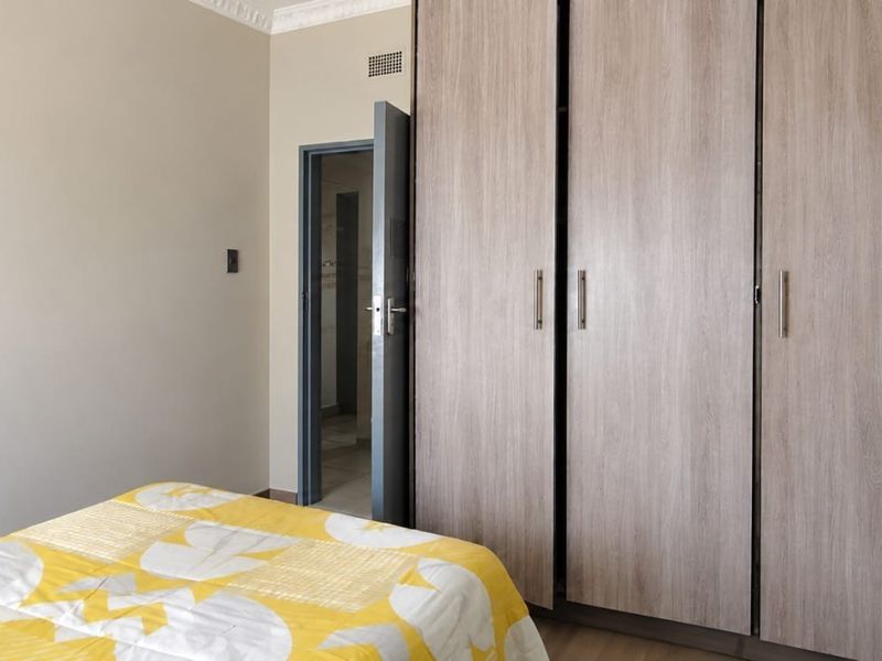 A bedroom featuring light wood-finish built-in cupboards, decorative ceiling cornice, and laminate flooring, with an adjacent doorway leading to an en-suite or hallway.