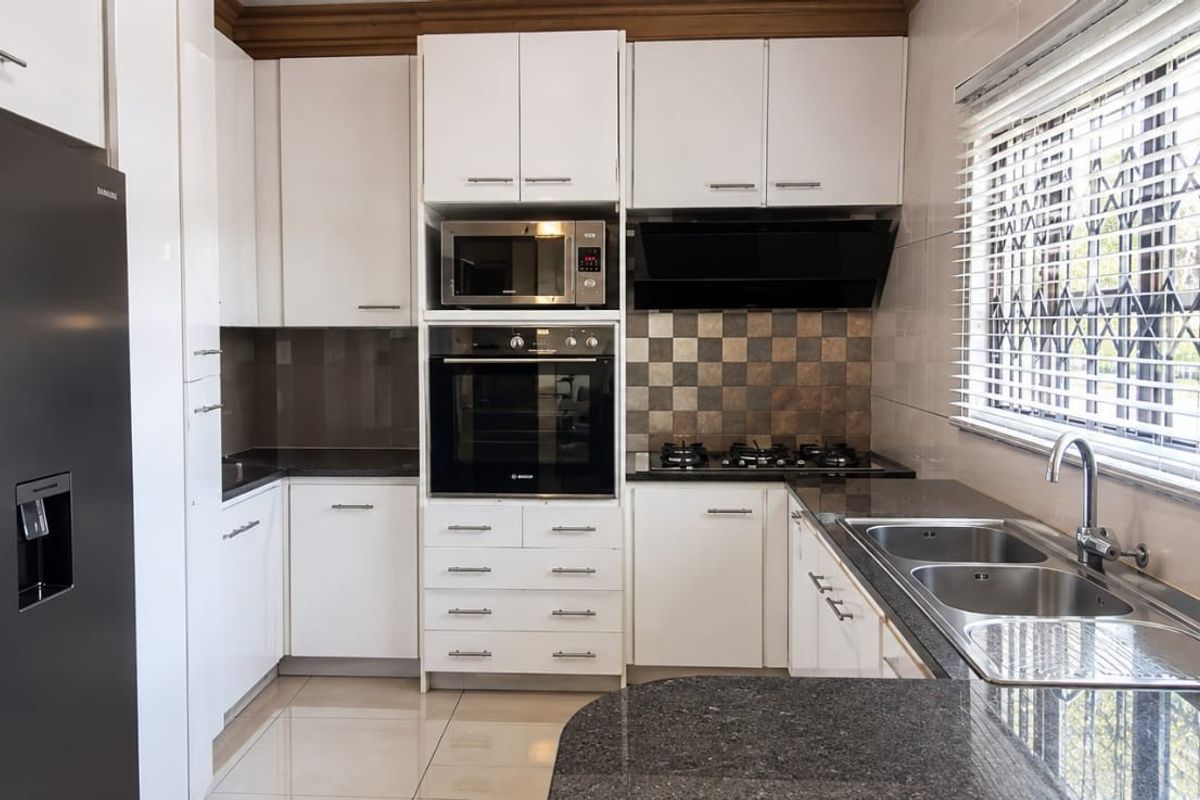 Modern kitchen featuring white cabinetry, granite countertops, built-in oven, microwave, gas hob, and a double sink with tiled backsplash and flooring.