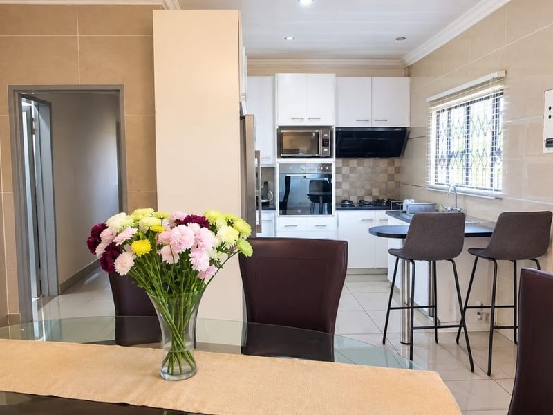 Modern open-plan kitchen and dining area featuring tiled finishes, built-in appliances, and a breakfast bar, creating a functional and cohesive living space.