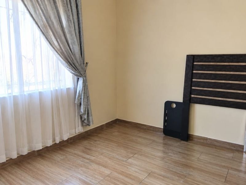 A bright and spacious bedroom featuring modern tiled flooring and a large window, providing a clean and neutral canvas for personalization.