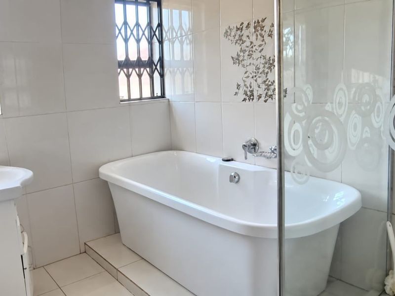 A clean, well-maintained bathroom featuring a freestanding bathtub, vanity basin, and a glass shower screen with decorative tiling.