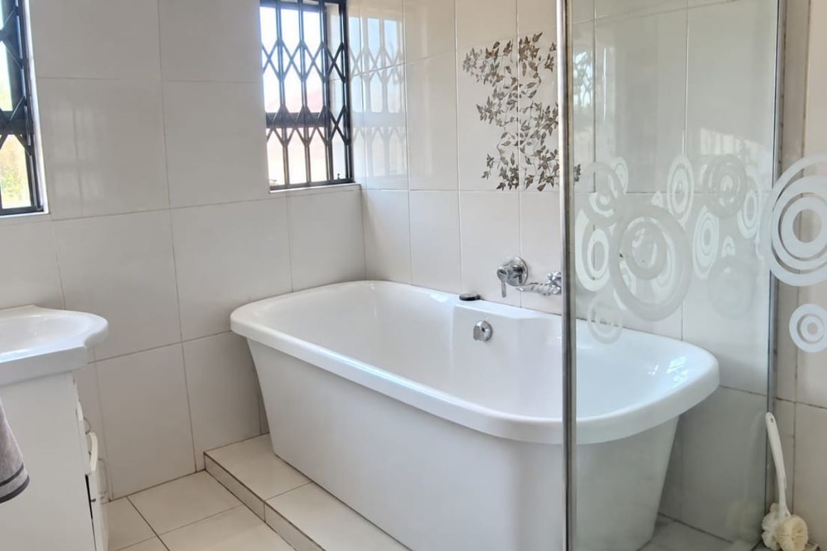 A clean, well-maintained bathroom featuring a freestanding bathtub, vanity basin, and a glass shower screen with decorative tiling.