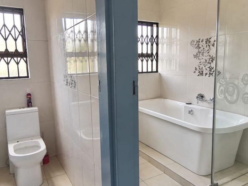 A clean, functional bathroom featuring a freestanding bathtub, a separate toilet area, and tiled finishes with decorative accents.