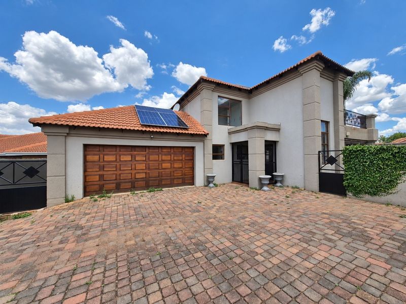Front elevation of a double-story house featuring a paved driveway, double garage with wooden door, and installed solar panels on the tiled roof.