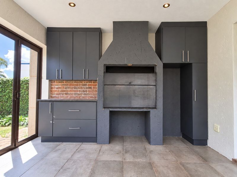 Covered patio area featuring a modern built-in braai, dark grey cabinetry, and tiled flooring with direct access to the garden through sliding glass doors.