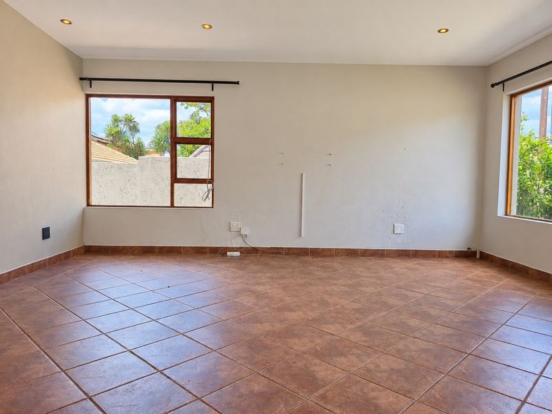 A spacious, empty living area featuring neutral walls, tiled flooring, and large windows that provide ample natural light.