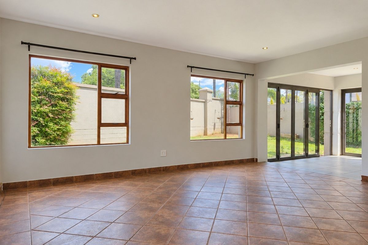 Spacious, light-filled living area featuring neutral walls, tiled flooring, and large windows with direct access to the outdoor patio and garden.