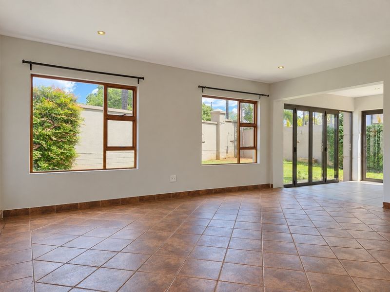 Spacious, light-filled living area featuring neutral walls, tiled flooring, and large windows with direct access to the outdoor patio and garden.