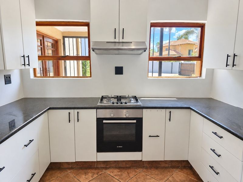 Modern kitchen featuring white cabinetry, dark stone countertops, a gas hob, built-in oven, and extractor fan, with natural light from dual windows.