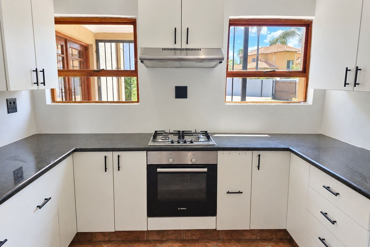 Modern kitchen featuring white cabinetry, dark stone countertops, a gas hob, built-in oven, and extractor fan, with natural light from dual windows.