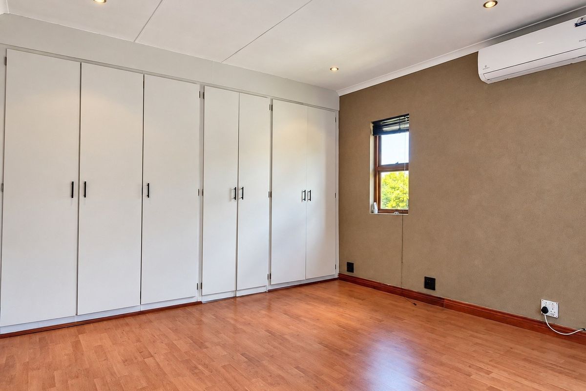 A bright, empty bedroom featuring extensive built-in cupboards, laminate flooring, and a wall-mounted air conditioning unit.