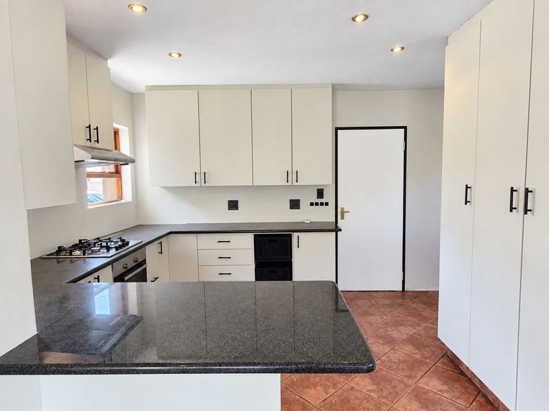 A clean, modern kitchen featuring granite countertops, built-in oven, gas hob, extractor fan, and ample storage cabinetry with tiled flooring.