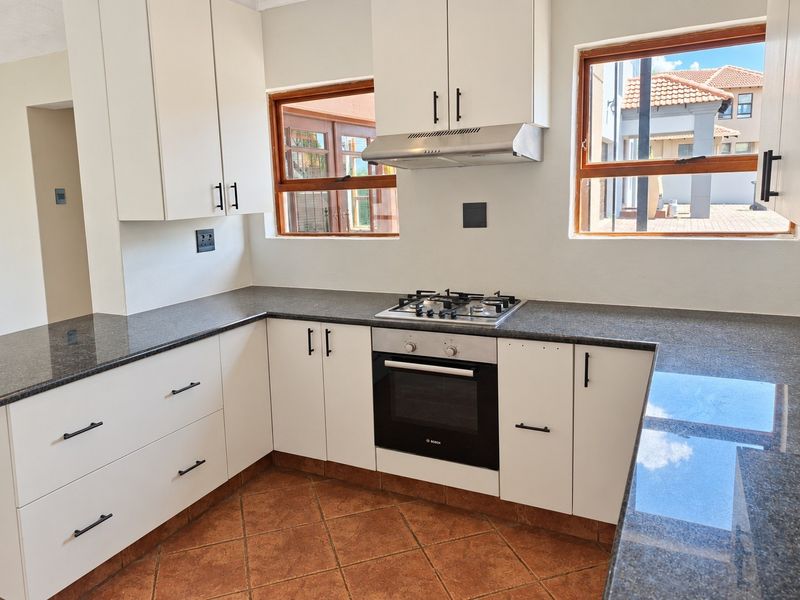 A clean, modern kitchen featuring white cabinetry, dark granite countertops, a built-in oven, gas hob, and an extractor fan.