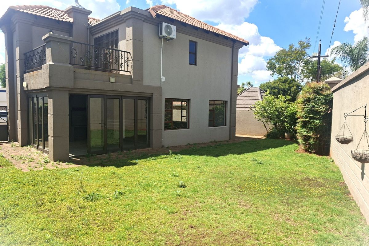 Rear view of a two-story house featuring a balcony, sliding glass doors, and a private garden with a perimeter wall.