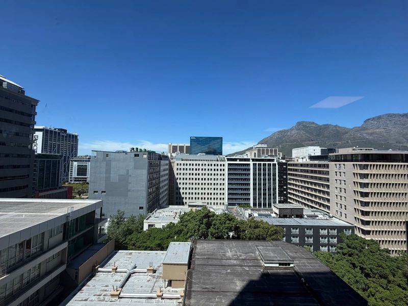 An elevated city view showcasing surrounding office buildings and a mountain backdrop under a clear blue sky.
