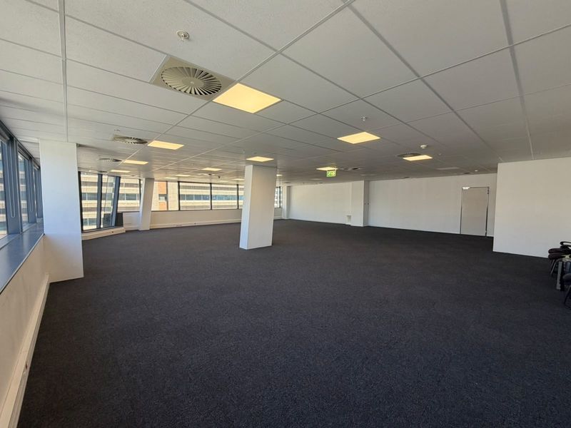 Spacious open-plan office area featuring a suspended ceiling, recessed lighting, central air conditioning, and large windows providing ample natural light.