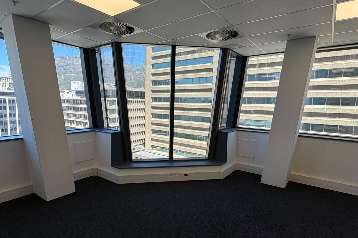 A bright, empty corner office space featuring large windows with city views, suspended ceilings, and dark carpeting, suitable for a professional workspace.