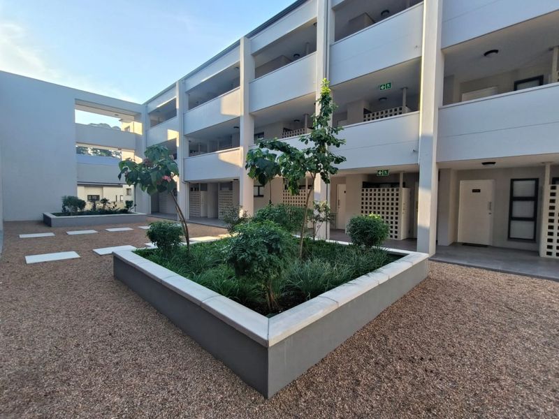 A well-maintained apartment complex courtyard featuring modern concrete architecture, gravel landscaping, and elevated walkways providing access to individual units.