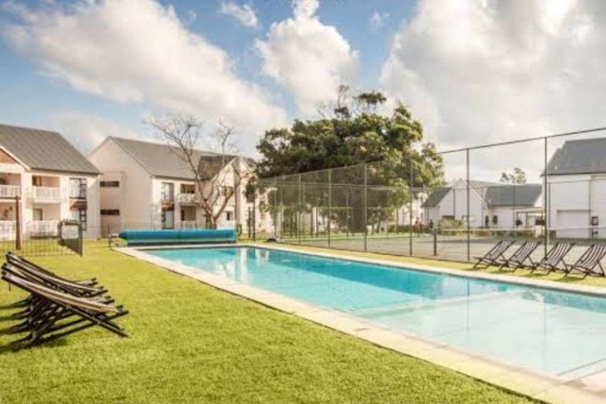 Communal outdoor area featuring a swimming pool and tennis court set within a landscaped residential estate.