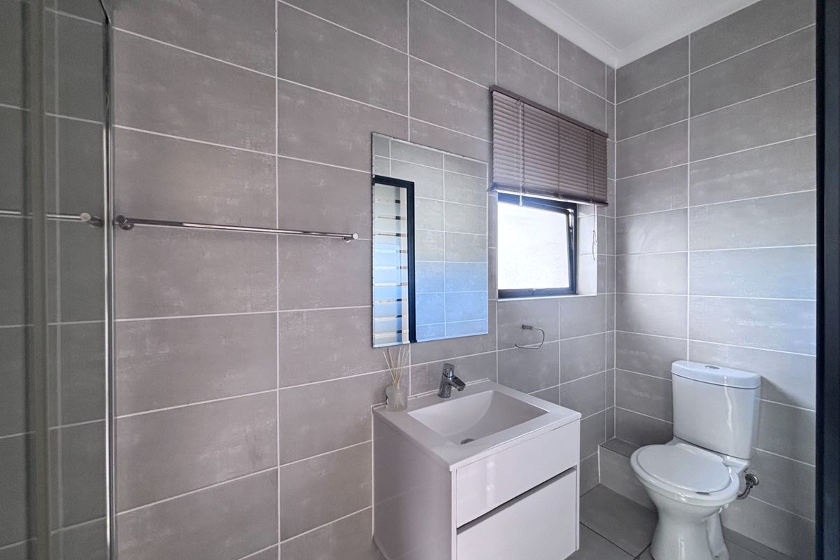 Modern bathroom featuring full-height grey wall tiling, a sleek wall-mounted vanity, a white ceramic toilet, and a glass-enclosed shower area.