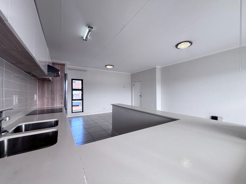 A bright, modern open-plan kitchen and living area featuring sleek cabinetry, a breakfast counter, and neutral tiled flooring throughout.