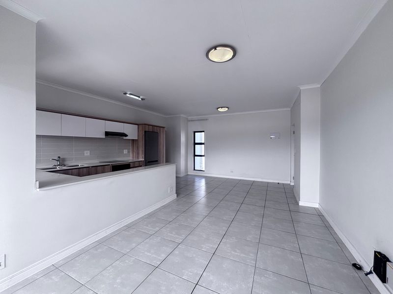 Spacious open-plan living and kitchen area featuring modern cabinetry, tiled flooring, and neutral finishes, providing a versatile blank canvas for interior design.