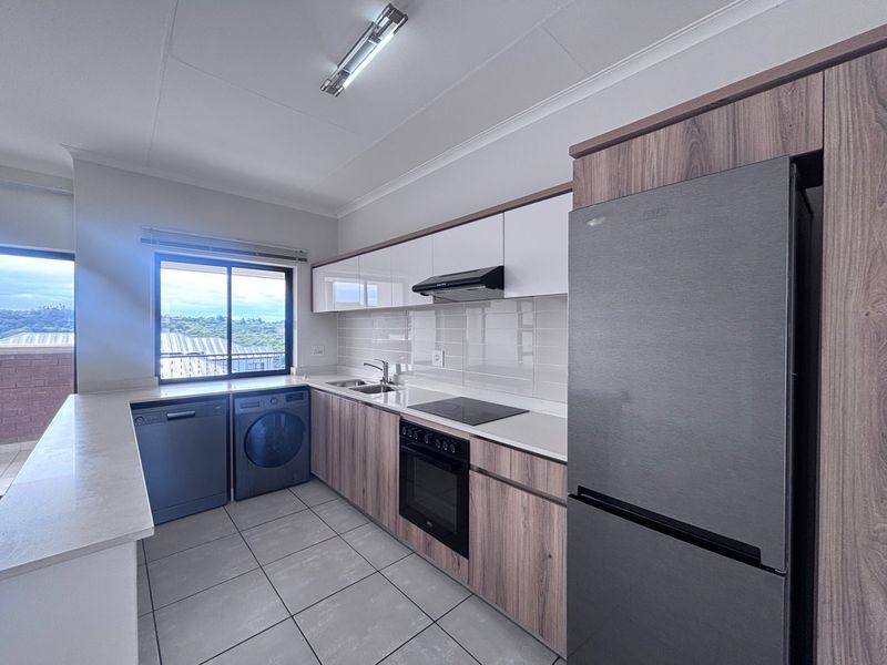 Modern kitchen featuring wood-grain cabinetry, stone countertops, tiled backsplash, and integrated appliances, offering a clean and functional workspace with ample storage.