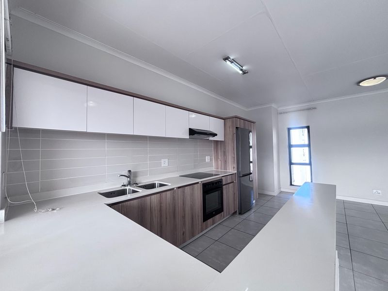 Modern kitchen featuring sleek white and wood-grain cabinetry, stone countertops, integrated appliances, and a functional breakfast bar layout.